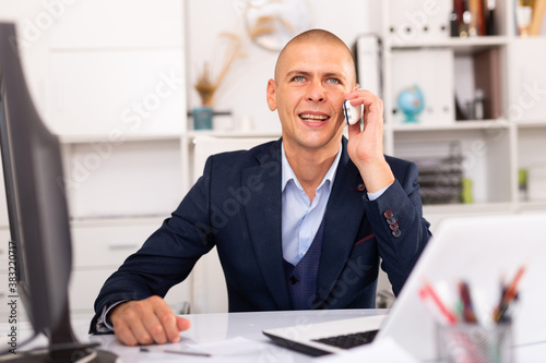 Positive man in formalwear talking on mobile phone at company office