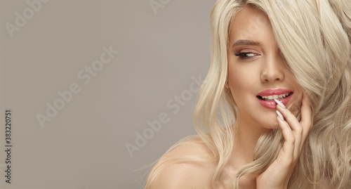 Luxury close up portrait of caucasian smiling woman with perfect curly blonde hair and makeup, looks away on beige background