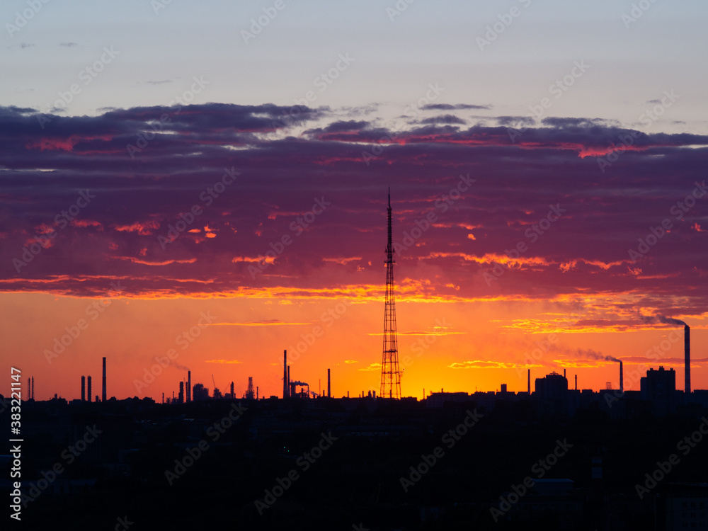 TV tower at sunset, as well as the factory outlines of an oil refinery in the rays of sunset. Outlines of the pipes of factories.