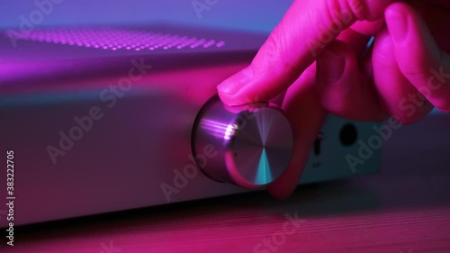Hand twists the amplifier button. Female turn on tumbler increasing music volume on amp. Close up view in neon light