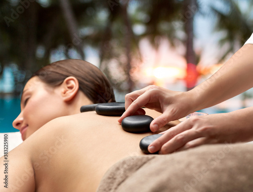 wellness, beauty and bodycare concept - close up of woman having hot stone massage at spa over tropical beach background in french polynesia photo