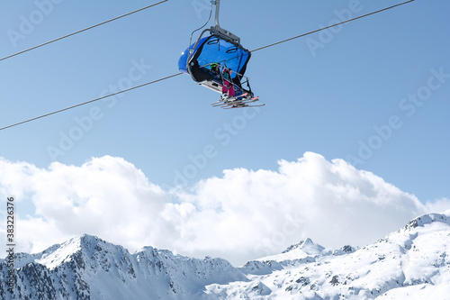 A view of the snow-capped mountains and the cable car with blue chair cabins in which children ride. Concept for sports, landscape, technology.
