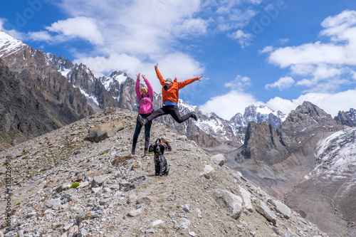 Not young spouses and their dog climbed to a height of 3300 meters above sea level. They are very happy that they were able to go so far. They jump, laugh against the background of snowy mountains.