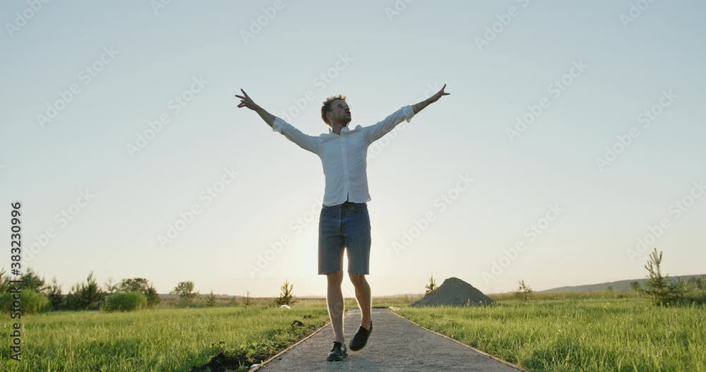 Tracking shot of happy young male walking on path and gesticulating against sunset sky in countryside Tracking shot of happy young male walking on path and gesticulating against sunset sky in countryside