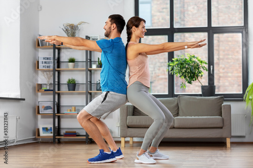 sport, fitness, lifestyle and people concept - smiling man and woman exercising and doing squats at home