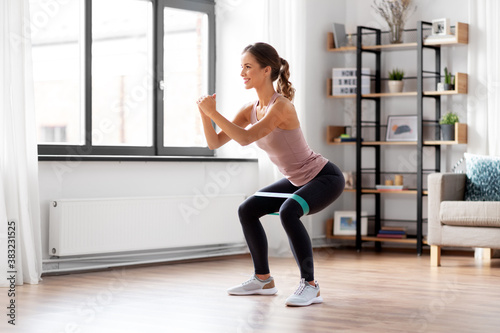sport, fitness and healthy lifestyle concept - smiling young woman with resistance band exercising and doing squats at home