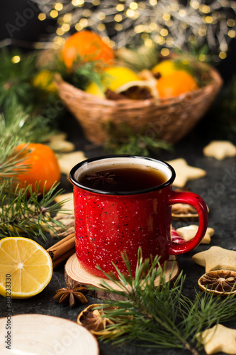 hot tea in a red mug in a new year s atmosphere. Christmas morning. A mug with a drink next to Christmas tree branches  oranges  spices and cookies