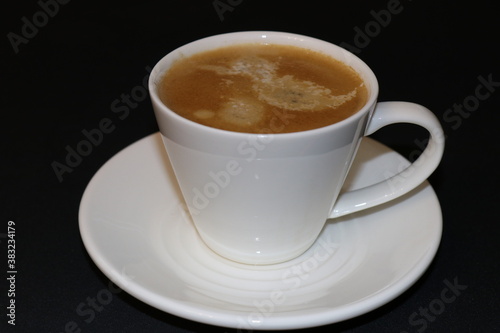 Cup of coffee in a white cup on a saucer on a black background