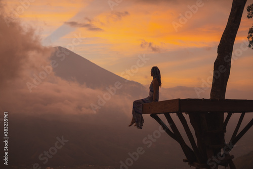 Silhouette of a girl in a long dress sitting near Bali landmark volcano Agung view. Travel blogger, Indonesia best sunset point destination. Woman retreat. High quality photo