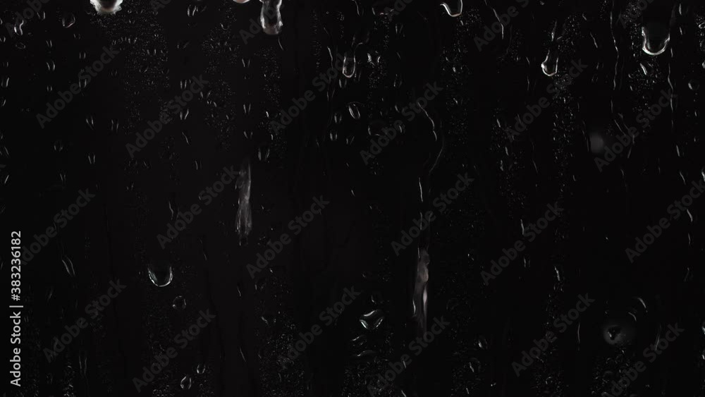Rain drops falling down on window over black background, raining at night, 4K