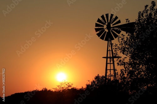 windmill at sunset with the sun and tree's out in the country north of Hutchinson Kansas USA.