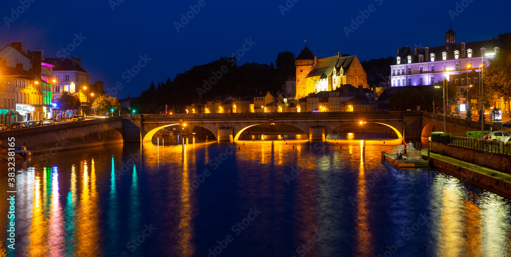 Scenic view of lighted ancient Laval castle on banks of Mayenne river at summer dusk, France