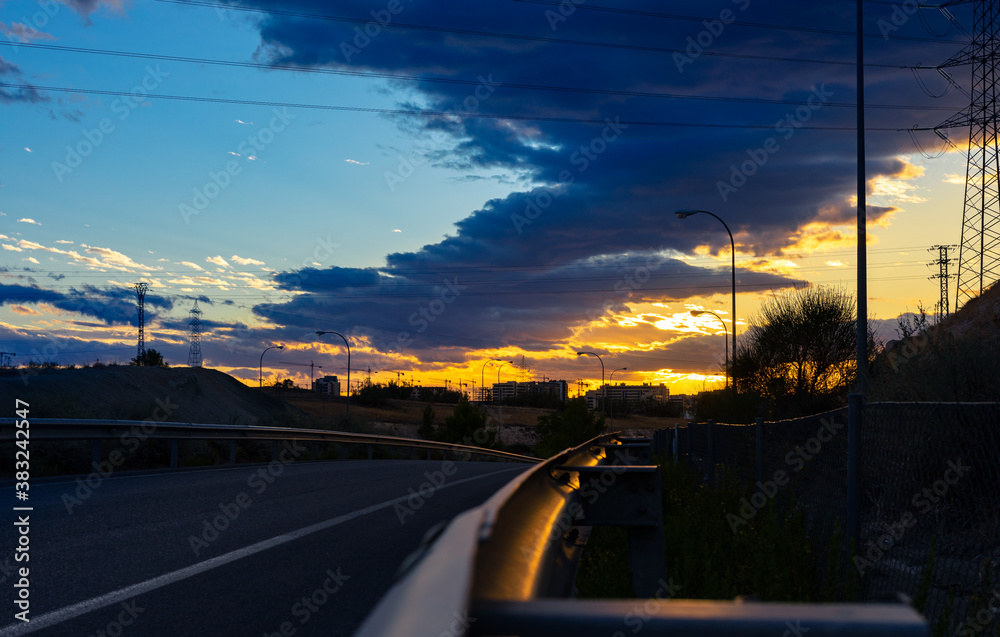Yellow light illuminates a guardrail on a road in Spain, and you can appreciate the detail of how sharp it is, with the danger it entails for motorists. You can also see cranes and constructions in th