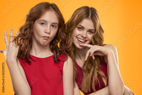 A red-haired girl and a beautiful woman on a yellow background in red dresses gesticulate with their hands and grimace