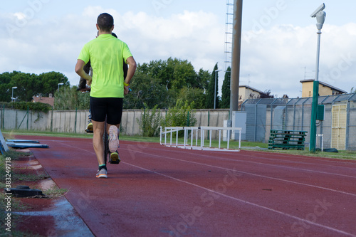 Two men training on a training track. One is running and the other is cycling. © Patricio