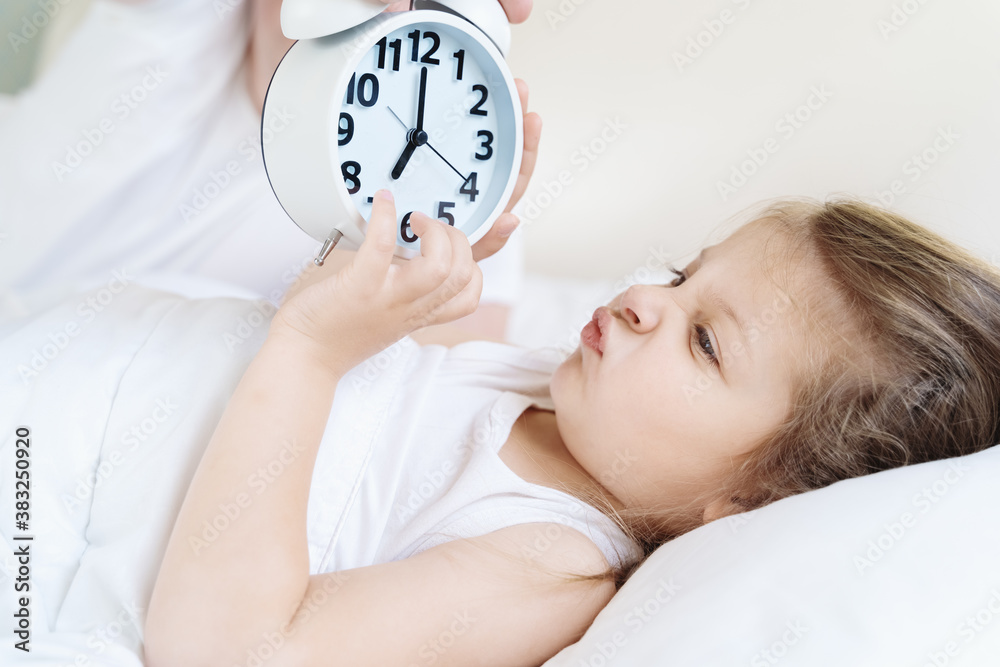 Dad wakes up little sleeping in bed girl,daughter. Big alarm,clock. Early morning before kindergaten, school. White pillow, blanket in bed. Sleepy child.Displeased, sad, unhappy.Bedtime.Daily routine Dad wakes up little sleeping in bed girl,daughter. Big alarm,clock. Early morning before kindergaten, school. White pillow, blanket in bed. Sleepy child.Displeased, sad, unhappy.Bedtime.Daily routine
