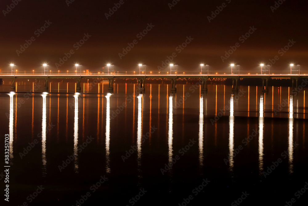 Obraz premium The night bridge with beautiful lanterns is reflected in the water on the River. Evening river landscape in a big city. Dnepropetrovsk, Dnipro city, Ukraine.