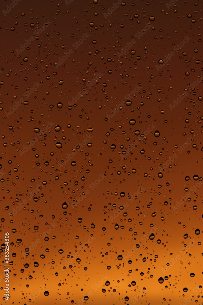 Rain drops on the window. Drops of water on glass, yellow and orange sunset in background.