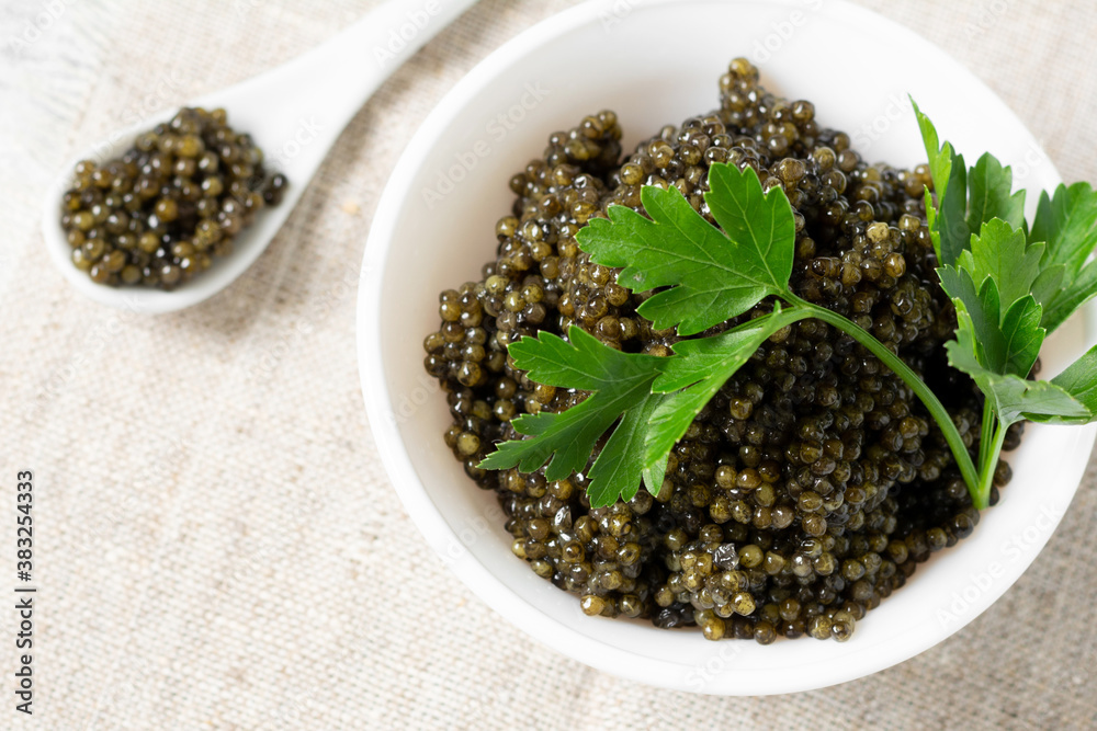 Black caviar. Black sturgeon caviar in a ceramic bowl and in a ceramic spoon on a light background. Useful delicacy. Top view with space for text Black caviar. Black sturgeon caviar in a ceramic bowl and in a ceramic spoon on a light background. Useful delicacy. Top view with space for text