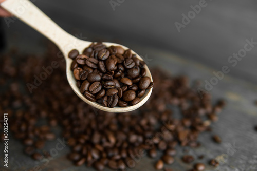 Fresh roasted arabica coffee beans in a wooden spoon and scattered coffee beans on a wooden table.