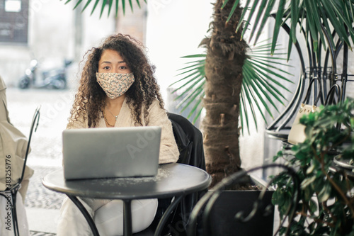 Young woman with a virus-mask is working sitting in a bar with her laptop