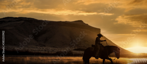 The silhouette of a cowboy on a horse with golden sunset landscape.