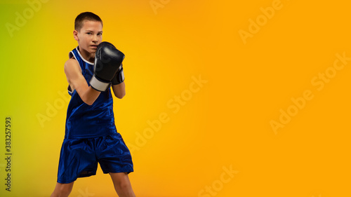 Competitive. Teenage professional boxer training in action, motion isolated on gradient background in neon light. Kicking, boxing. Concept of sport, movement, energy and dynamic, healthy lifestyle.