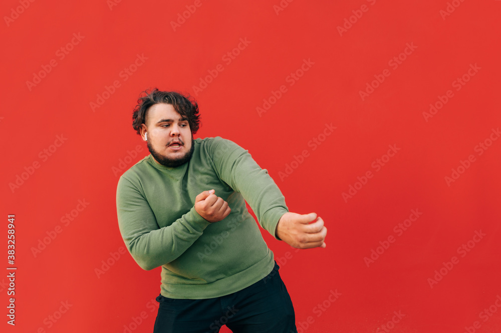 Charismatic overweight man with curly hair dancing on red background and looking away at copy space isolated on red background. Charismatic overweight man with curly hair dancing on red background and looking away at copy space isolated on red background.