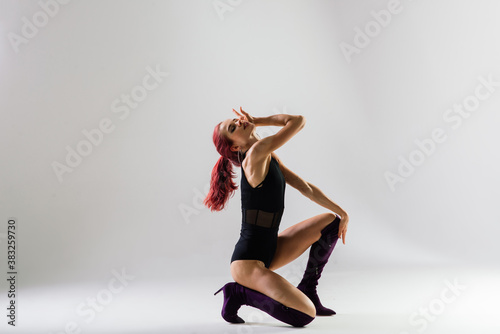 Young beautiful flexible female in black jumpsuit and high heels is posing in a dance studio.