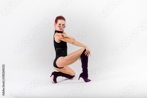 Young beautiful flexible female in black jumpsuit and high heels is posing in a dance studio.