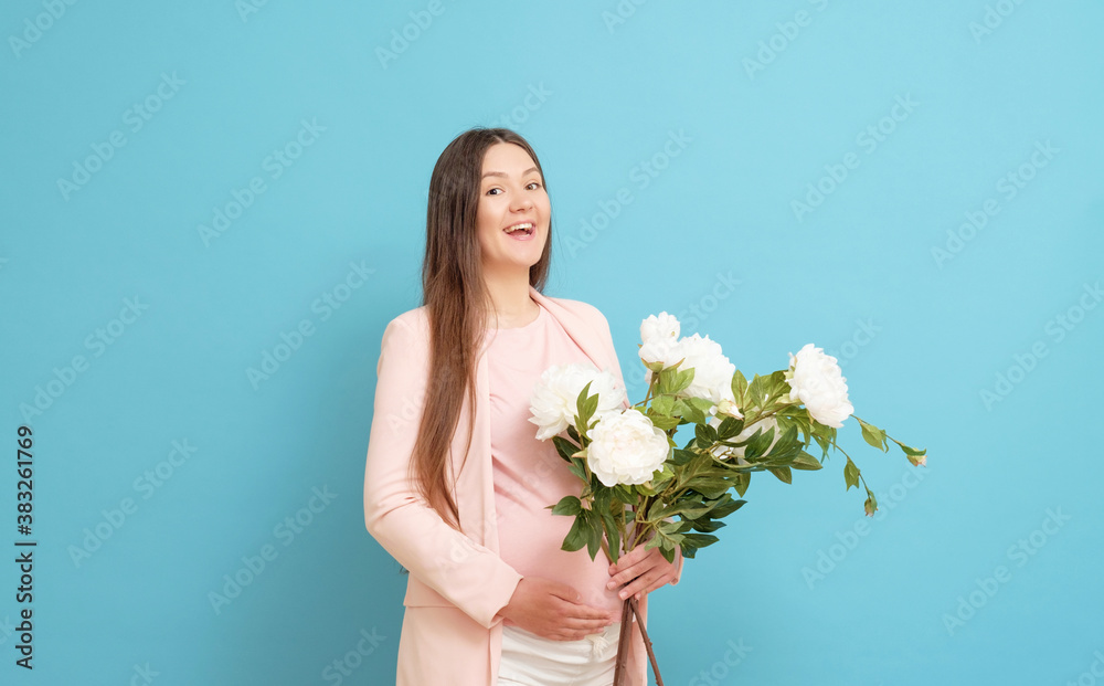 happy young pregnant woman in pink t-shirt on blue background holding a bouquet of flowers