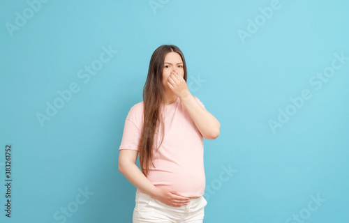 young pregnant woman in pink t-shirt on blue background, toxicosis during pregnancy © denisval