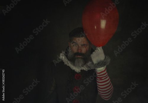 Evil and scary man holding red balloon in hand on black background .Halloween vintage costume. Painted Halloween holiday makeup.