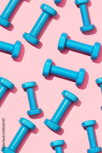Fitness dumbbells blue on a pink background pattern. Equipment for home workouts and exercises in the flat lay gym. Sports dumbbell for a healthy lifestyle top view. photo