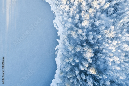 Аerial view of snow covered forest around beautiful lake. Rime ice and hoar frost covering trees. Scenic winter landscape. Copy space. Christmas concept.