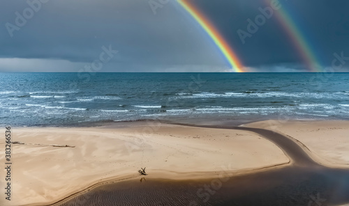 Colorful rainbow and rain over a sandy beach and estuary of small stream at t...