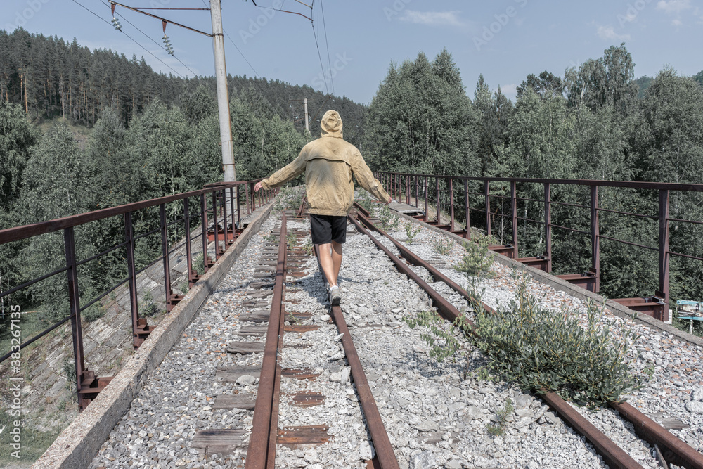 a man walks across an abandoned railway bridge. old iron bridge in the forest across the road. a man walks across an abandoned railway bridge. old iron bridge in the forest across the road.
