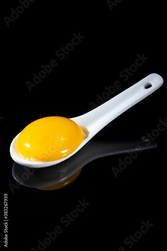 Egg yolk in a white spoon on a black background. Close up. Reflection.