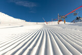 Close-up straight line rows of freshly prepared groomed ski slope piste with bright shining sun and clear blue sky background. Snowcapped mountain downhill landscape at europe winter skiing resort