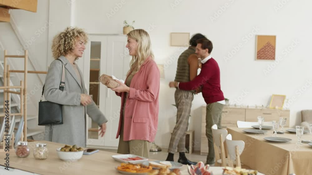 Pan shot of Caucasian couple greeting their diverse friends coming for dinner with gifts for Thanksgiving Day Pan shot of Caucasian couple greeting their diverse friends coming for dinner with gifts for Thanksgiving Day