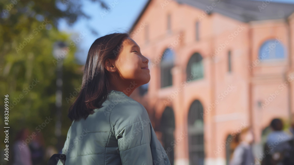 Back view of happy asian schoolgirl standing near building happy to come back after summer holidays