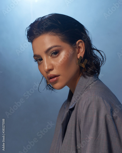 Closeup fashion face studio portrait. Tanned caucasian brunette woman. Fashionable stylish female model with makeup and wet hair against smoke at background photo
