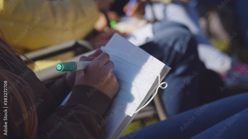 Close up of schoolgirl sitting outdoors and painting safety mask with marker