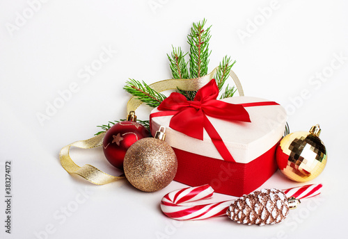 On a white background lies a gift with a red bow, Christmas balls, green spruce branches and a lollipop cane. Christmas decor. Christmas concept
