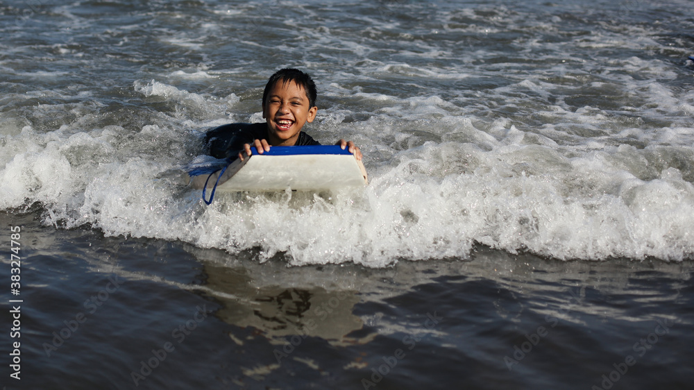 Boy has fun riding waves into shore. Playing at the beach. Kid surfer. Boy has fun riding waves into shore. Playing at the beach. Kid surfer.