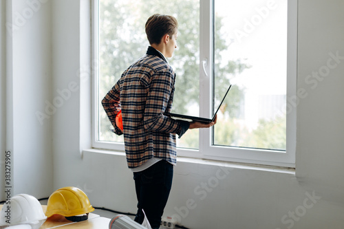 Rear view of young, professional business guy working with laptop near window