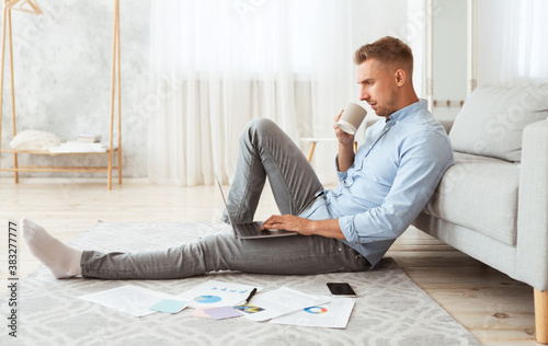 Focused man sitting on floor using phone drinking coffee