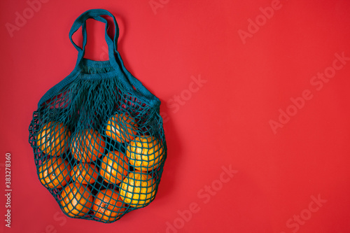 Fresh tangerines in a cotton string bag on a green background. Christmas. Flat lay, top view, copy space. Focus on bag