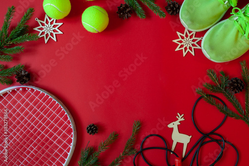 Tennis Christmas, Happy New Year concept with tennis ball as Christmas tree toy decoration and fir tree branches on red background. Winter sport healthy ornament. Flat lay, top view, copy space.