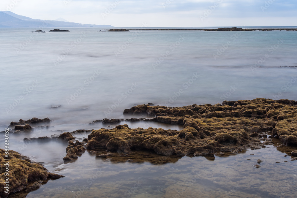 Stones covered by moss form ponds with the calm sea protected by barrier reefs.